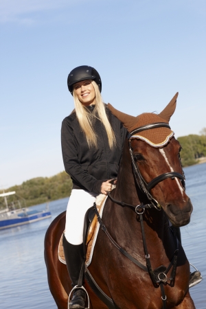 Blonde horsewoman riding horse at riverside looking away.の写真素材