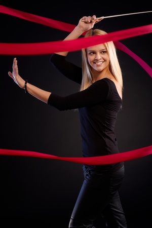 Beautiful female dancer using ribbon, smiling happy over black background.の写真素材