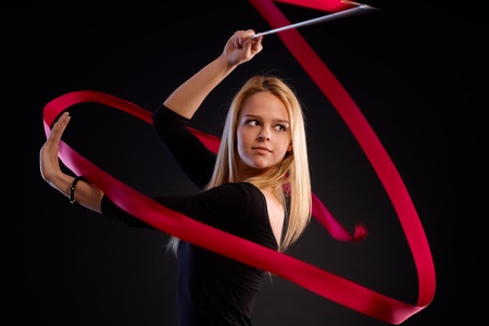 Young rhytmic gymnast using ribbon, looking away, over black background.の写真素材
