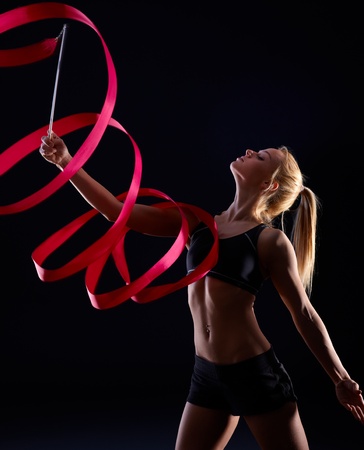 Artistic photo of pretty female dancer using ribbon, exercising over black background.の写真素材