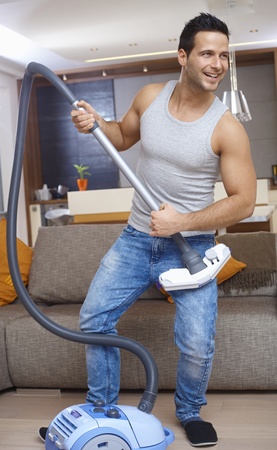 Young man holding vacuum cleaner as guitar, having fun at home, smiling.の写真素材