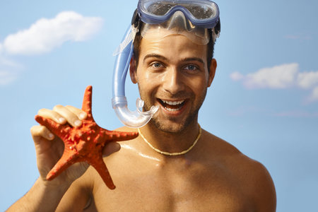 Portrait of happy young scuba diver holding starfish at summertime. 