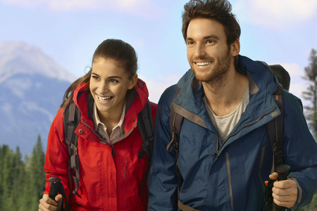 Young hiking couple trekking in mountains, climbing uphill, smiling. 