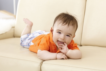 Beautiful baby boy lying on sofa, smiling happy with hand in mouth.の写真素材