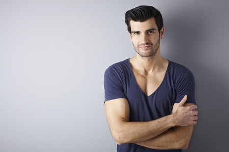 Portrait of handsome young man standing arms crossed by wall, smiling, looking at camera.の写真素材