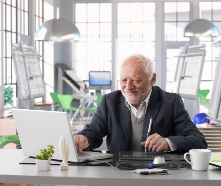 Senior engineer sitting at desk doing design work with computer at architect studio.の写真素材