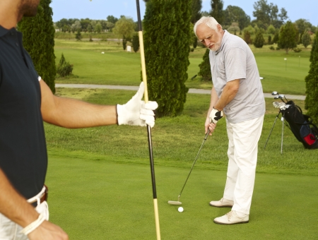Senior golfer standing on the green ready for holing.の写真素材