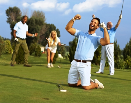 Happy golfer kneeling at hole with raised fists after putting in golf ball to the hole.の写真素材