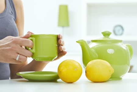 High key still life with tea kettle mug and lemon, pastel colors. Close up hand with ring, holding cup, copyspace.の写真素材
