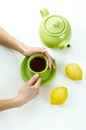 Female hand holding tea cup with kettle lemon high angle, high key. Pastel colors, white background.の写真素材