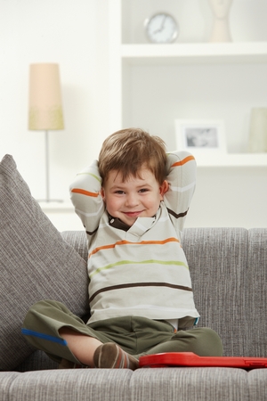 Portrait of smiling caucasian kid sitting on sofa at indoor home. Looking at camera.の写真素材