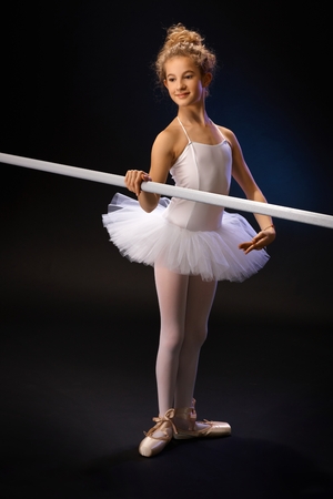 Smiling young ballet student practicing by ballet bar over black background.の写真素材