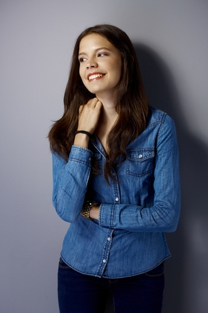 Happy girl leaning against grey wall, looking away.の写真素材