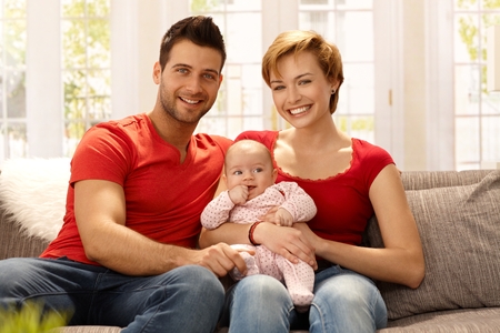 Happy young married couple holding baby girl on lap, smiling, looking at camera.の写真素材