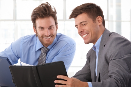 Happy, handsome caucasian businessman looking at personal organizer at business office. Smiling, wearing suit.の写真素材