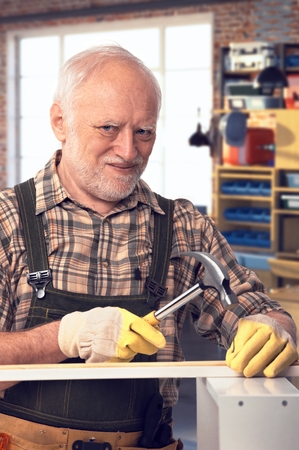Happy caucasian pensioner hammering at DIY home workshop. Looking at camera, smiling.の写真素材