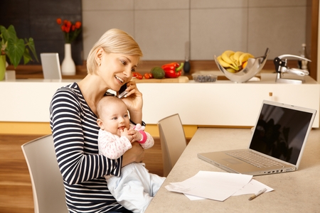 Young mother working from home, holding baby on lap.の写真素材