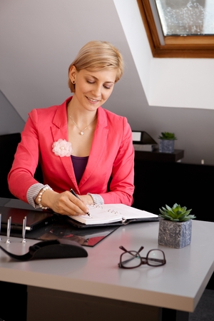 Portrait of businesswoman sitting at desk, working, writing notes.の写真素材