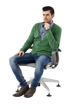 Handsome young businessman sitting and thinking in swivel chair over white background, looking away. Full size.