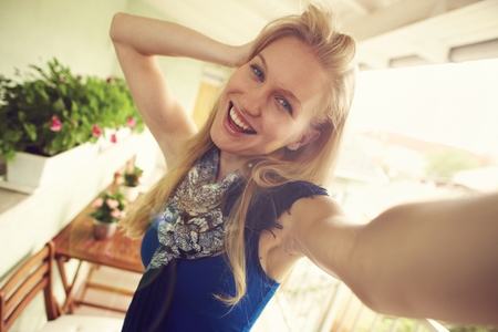Happy nordic woman making selfie at balcony in summertime, smiling, hand in hair.の写真素材