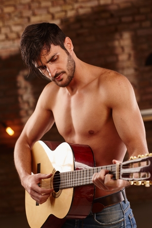 Romantic young man playing the guitar with bare upper body.の写真素材
