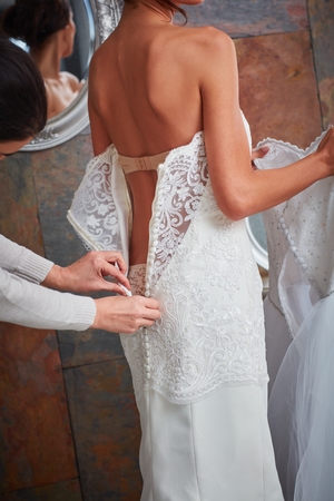 Female friend fastening buttons on wedding dress, photographed from behind.の写真素材