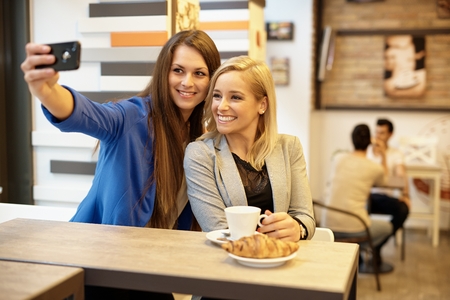 Happy attractive girls making self portrait by mobilephone in cafeteria.の写真素材