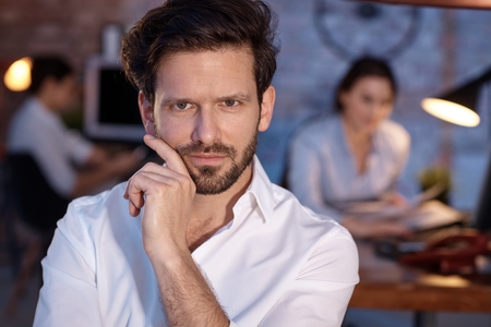 Closeup portrait of confident young businessman, looking at camera, hand on chin.の写真素材