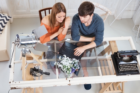 Young couple using laptop at home, sitting at desk. Above view.の写真素材