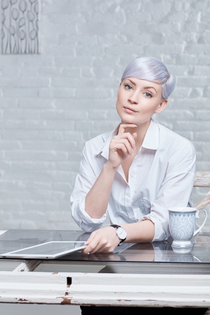 Portrait of young woman with extravagant hair sitting at desk, holding tablet computer.の写真素材