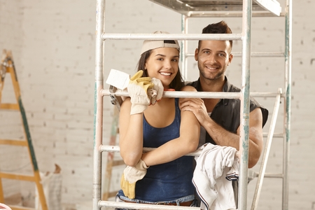 Happy young loving couple renovating home, embracing under scaffold, looking at camera.の写真素材