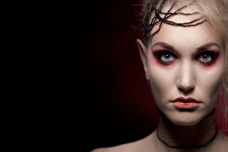 Young blonde woman wearing halloween makeup, looking at camera over black background.の写真素材