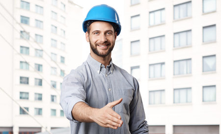 Happy young engineer offering handshake completed new building in background.