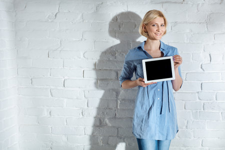 Happy woman holding tablet computer with blank screen, smiling, looking at camera.