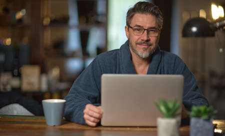 Businessman in home office wearing bathrobe working with laptopの写真素材
