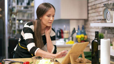 Woman cooking in kitchen at home reading recipe on tabletの写真素材