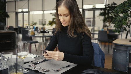 Happy woman using phone in restaurant or cafeの写真素材
