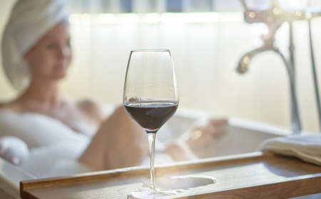 Woman relaxing in bubble bath in bathtub drinking wineの写真素材