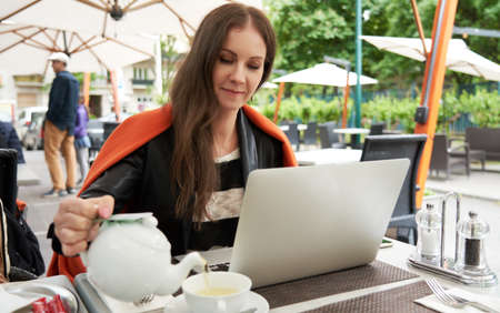 Woman drinking tea and working with laptop on cafe terraceの写真素材