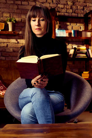 Young woman reading book in cosy dark roomの写真素材