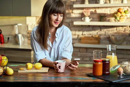 Woman using phone in kitchen at morningの写真素材