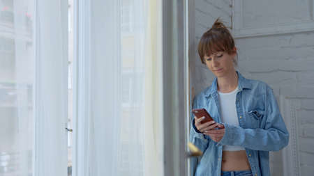 Woman at home at morning checking phone in windowの写真素材