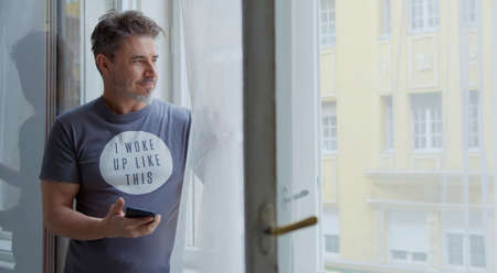 Man at home at morning checking phone in windowの写真素材