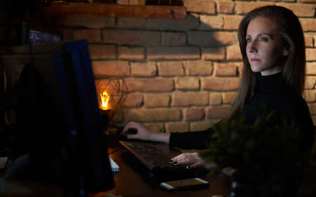 Woman working with computer in dark officeの写真素材
