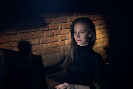 Woman working with computer in dark room at homeの写真素材