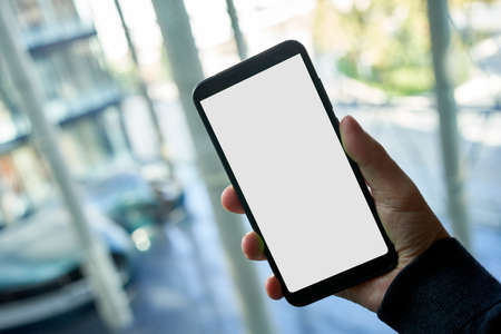 Hand holding phone with blank screen in officeの写真素材