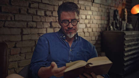 Mature man reading book at home in dark room.の写真素材