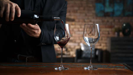 Man pouring red wine to wine glasses at homeの写真素材
