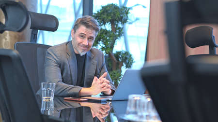 Older businessman working with laptop computer in office meeting room, smiling.の写真素材