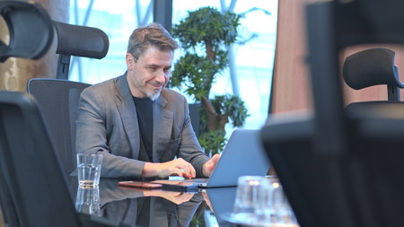 Older businessman working with laptop computer in office meeting room, concentrating.の写真素材